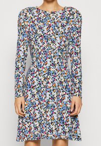 Kwiecista sukienka z długim rękawem, z granatowym tłem i wielobarwnymi kwiatami, dopasowaną talią oraz rozkloszowanym dołem, wykonana z lekkiego materiału.