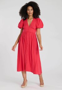 Röd bomulls-middklänning med puffärmar, djup V-ringning, knappstängning fram och en flödig A-linjeform. Slät textur med subtila veck.