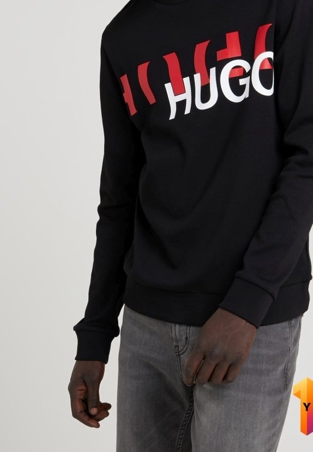 Sweatshirt noir avec un texte "HUGO" en rouge et blanc en grand format. Manches longues avec des poignets et un ourlet côtelés. Le tissu semble lisse avec une coupe décontractée.