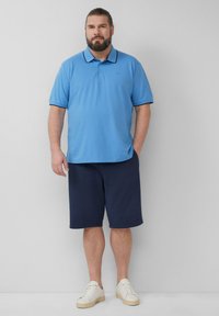 Lichtblauwe poloshirt met een kraag en marineblauwe details, gecombineerd met marineblauwe korte broek. Witte sneakers maken de outfit af. Casual ontwerp en pasvorm.
