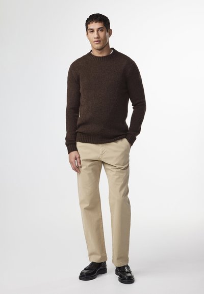 Bruine gebreide trui met een ronde hals, gecombineerd met beige chino's en zwarte leren schoenen. Soepele textuur, aansluitend design en neutrale kleuren.
