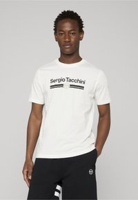 Hvid bomuld t-shirt med korte ærmer, der har en sort og guldfarvet "Sergio Tacchini"-logo og vandrette striber tværs over brystet.