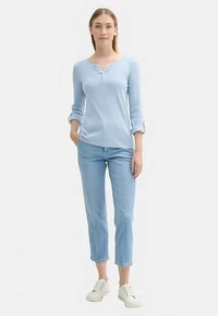 Svetlomodro dolgo rokavno majico s henley ovratnikom. Kombinirana s svetlo pranim kratkim jeans hlačami in belimi supergami. Gladek material z zavihanim rokavi.