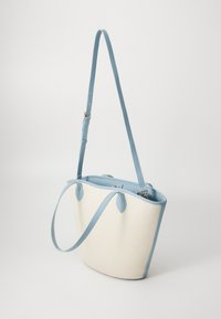 Canvas tote bag with a cream body, light blue leather trim and handles; includes round accents and adjustable shoulder strap.