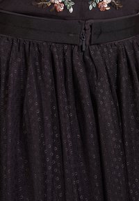 Jupe noire en tissu texturé avec un motif à pois. Elle présente une taille ajustée avec une fermeture éclair lisse à l'arrière.