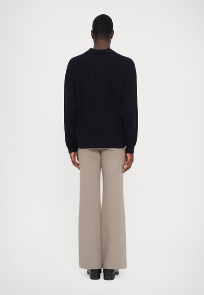 Navy ribbed sweater with a round neck, paired with light gray flared trousers. Black footwear is visible at the bottom.