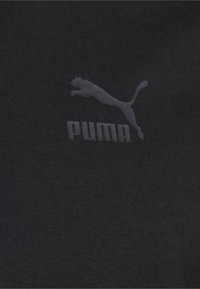 Tissu en coton noir avec une texture subtile, arborant un logo Puma blanc et du texte, centré sur la zone de la poitrine d'un t-shirt.