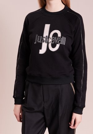 Schwarzer Hoodie mit einem cropped Design, ausgestattet mit grauer "Justcavalli" Schriftzug, silbernen Nieten sowie gerippten Bündchen und Saum. Glatte Textur.