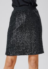 Jupe mini en sequins noirs avec une taille ajustée, pr�ésentant un motif vertical, une texture réfléchissante et une finition en tissu lisse.