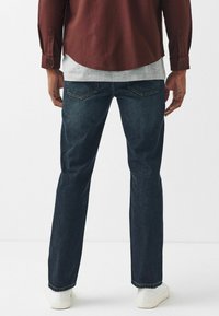 Vaqueros de mezclilla azul oscuro con corte recto, con bolsillos traseros y un acabado clásico, combinados con una camisa burdeos oscura.