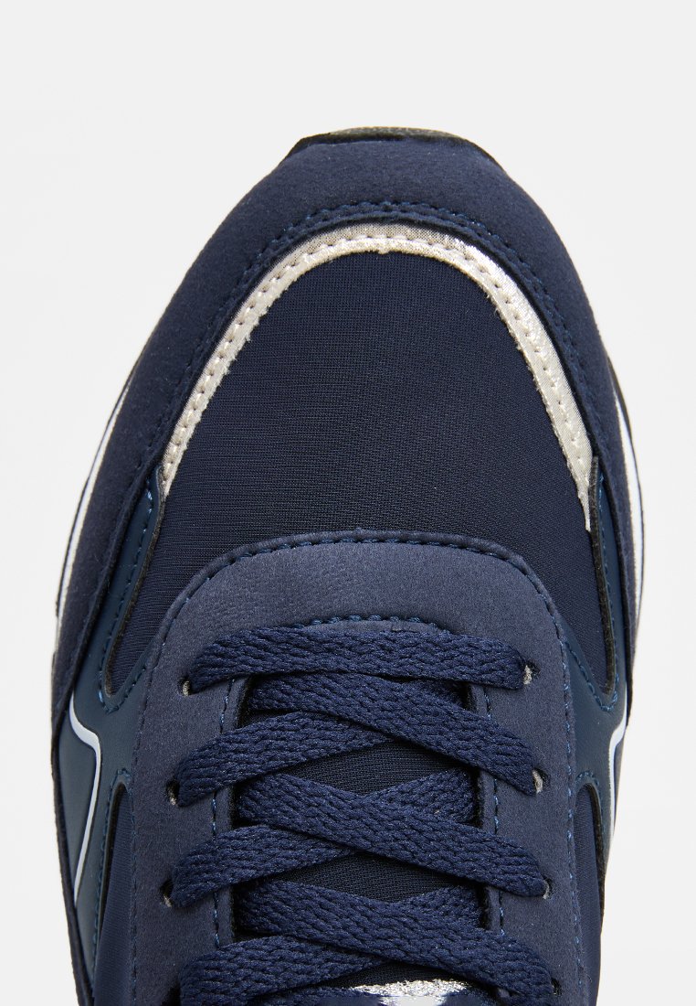 Zapatilla de deporte azul marino con un upper de tela texturizada, acentos plateados, cordones planos y un diseño de punta redonda con detalles cosidos.