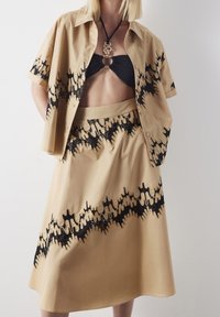 Beige set bestaande uit een short-sleeve shirt en rok, met zwarte abstracte patronen. Het shirt heeft een losse pasvorm en de stof is soepel.