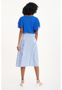 Top azul con mangas rizadas y puntadas, combinado con una falda blanca a la altura de la rodilla que presenta rayas verticales azules. Tela suave y diseño sencillo.