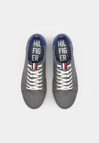 Grijze canvas sneakers met witte veters, blauwe accenten en een rood, wit en blauwe logo. Geïncludeerd zijn een gevoerde kraag en een gepatroonde binnenzool.