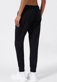 Zwarte katoenen joggers met elastische tailleband, taps toelopende broekspijpen en ribgebreide boorden. Draag ze met witte sport sneakers.
