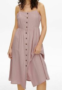 Ärmlös, knälång klänning i mjuk ljuslila linne med knapplist fram och rynkad midja. Har en avslappnad passform och subtil textur.