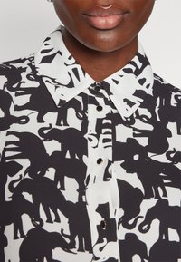 Black and white button-up shirt featuring a repeating elephant pattern, with a structured collar and smooth fabric texture.