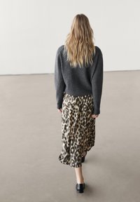 Szary, krótki sweter połączony z suknią w panterkę o długości do ziemi. Gładki materiał z lekko opadającym krojem. Czarne buty dopełniają stylizację.