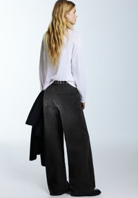 Čierne džínsové nohavice s širokými nohavicami a vysokým pásom, vybavené zadnými vreckami a opaskom s kovovými detailmi; skombinované s voľným bielym topom.