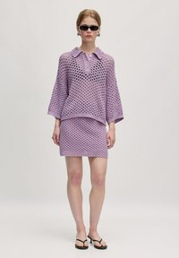 Lavendel brei set met een kortemouw, knoopsluiting bovenkant met een kraag en een bijpassende mini rok. Open geweven patroon met een relaxte pasvorm.