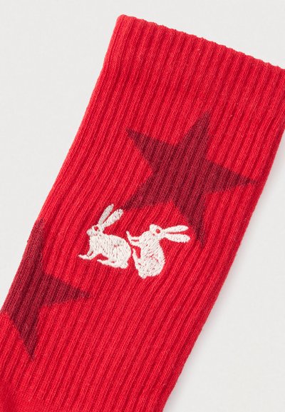 Κόκκινες ριγωτές κάλτσες με μεγάλο μαύρο αστέρι και δύο λευκά κεντημένα λαγουδάκια. Το υλικό φαίνεται μαλακό και ελαστικό.