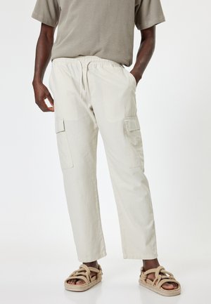 Beige cargobroek met een elastische tailleband en twee zijzakken. Gemaakt van lichtgewicht stof. Gecombineerd met tan gekleurde, gestructureerde sandalen.