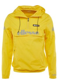 Coupe-vent léger jaune avec capuche, fermeture éclair devant, cordons et grand logo "ellesse" sur la patte de la poche poitrine et les manches.