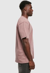 Heledane roosa lühikeste varrukatega T-särk, mugava lõikega, puuvillane materjal, nähtavad õmblused ja ümar kaelus, esitatud külgprofilis.