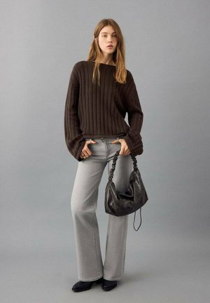 Brown ribbed sweater, gray flared jeans, black handbag with a twisted handle, and black shoes. Neutral background.