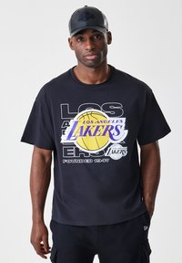 Čierne tričko s farebnou grafikou "Los Angeles Lakers" a ikonou basketbalu. Tričko je krátkopupinové a vyrobené z mäkkej látky.
