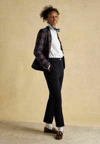 Pleds žakete ar tumši zaļām, sarkanām un dzeltenām akcentiem; balta krekls; melnas kordurošanas bikses; bordo loafer apavi ar zelta detaļām; īsas baltas zeķes.