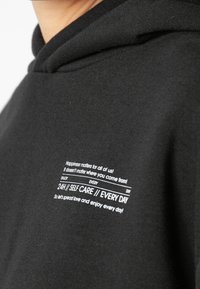 Zwarte hoodie met een zachte textuur, voorzien van witte tekst op de borst. De tekst bevat motiverende zinnen over zelfzorg en genot.