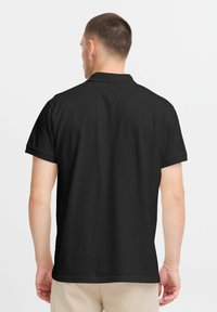 Sort polo skjorte med korte ærmer, ensfarvet, lavet af tekstureret stof, med klassisk krave og afslappet pasform. Ingen synlige logoer.