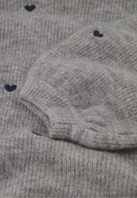 Grijze gebreide trui met ribbeltextuur en blauwe hartpatronen. Heeft een opgevouwen manchet en zacht, pluizig materiaal voor warmte.