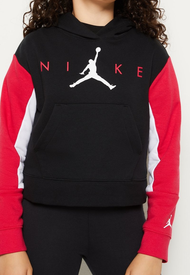 Bambino che indossa un felpa nera con maniche rosse e bianche, con il logo Jumpman bianco e la scritta NIKE rossa sul davanti.