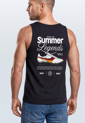 Man wearing black sleeveless shirt with "Summer Legends" and a soccer shoe graphic on the back, paired with blue jeans.
