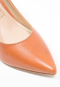 Chaussure à bout pointu en cuir beige avec une texture lisse, dotée d'un décolleté bas et d'une silhouette épurée. Couture discrète le long des bords.