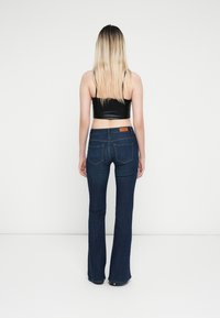Sötétkék farmer elágazó nadrág öt zsebes dizájnnal, finom varrásokkal és bőrből készült folttal a deréknál. Fekete, testhezálló crop top.