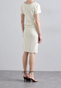 Krämfärgad kortärmad klänning med rund halsringning och figurnära silhuett. Kompletterad med svarta sandaletter med hög klack och remmar. Slät textur.