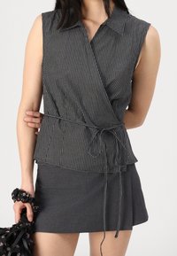 Top senza maniche a righe bianche e nere con colletto, design avvolgente e dettaglio in vita con fiocco, abbinato a una minigonna grigia.