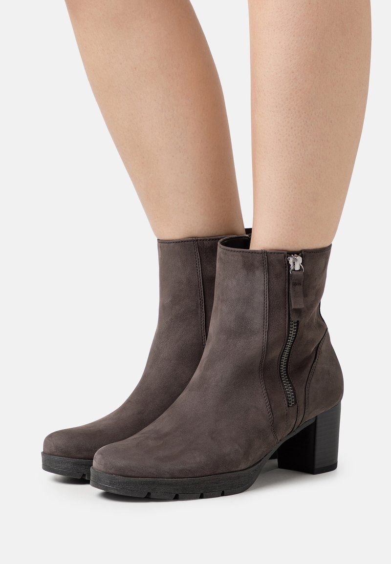 Bottes en daim marron jusqu'à la cheville avec fermeture éclair latérale et talons carrés, portées sur des jambes nues, vue de face et de côté.