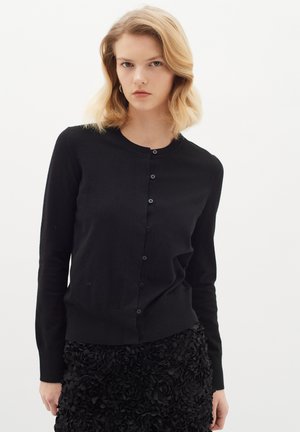 Black cardigan made of a soft material with a round neck, button-front closure, and long sleeves. Featuring a fitted design and ribbed hem.