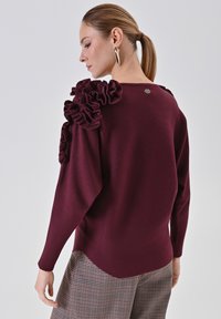 Maglione bordeaux con dettagli arricciati sulle spalle, maniche lunghe, scollo rotondo e un sottile logo sulla schiena.