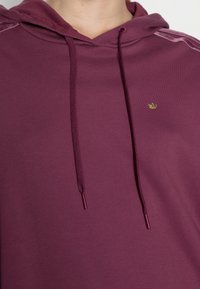 Bordeaux hoodie gjord av mjuk bomullsblandning. Har en justerbar huva, subtilt logotyp och sidostycke i en kontrasterande färg.