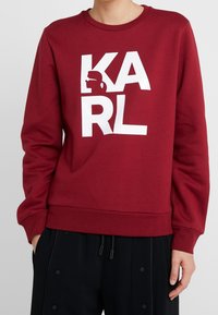 Burgundy sweatshirt med iögonfallande vit text "KARL" och grafisk profilDetalj. Tillverkad av bomull med rund halsringning och ribbad mudd.