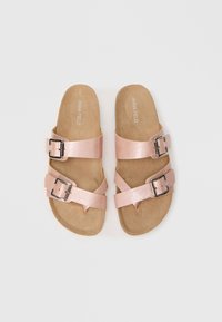 Ροζ δερμάτινα σαγιονάρες με δύο επικαλυπτόμενες λωρίδες, η καθεμία με μια ασημένια αγκράφα. Μαλακή καφέ σόλα, επίπεδη σχεδίαση και μινιμαλιστικό στυλ.