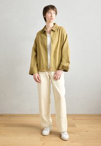 Olive green oversized jacket with a shirt collar, wide sleeves, front pockets, paired with cream wide-legged trousers and white sneakers.
