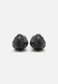 Zapatos de cuero negro tipo slip-on con punta redonda, superficie texturizada y diseño minimalista con suelas de perfil bajo.