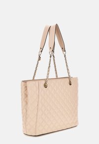 Gequilted beige tote bag met dubbele handvatten, kettingaccenten en glanzend gouden hardware. Gladde textuur, rechthoekige vorm en minimale details.