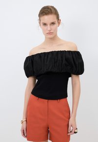 Top nero off-the-shoulder con maniche a sbuffo arricciate, abbinato a pantaloni corti arancioni. Tessuto liscio con design strutturato.